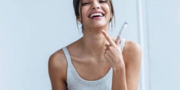 Shot of pretty young woman brushing her teeth while looking at camera in the bathroom at home.