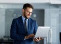 Smiling businessman working on a laptop in a modern office, confidently typing on the keyboard while enjoying a productive day