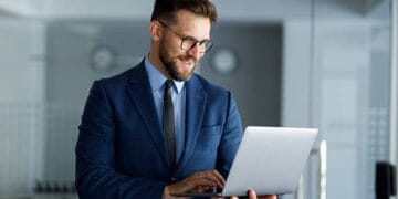 Smiling businessman working on a laptop in a modern office, confidently typing on the keyboard while enjoying a productive day