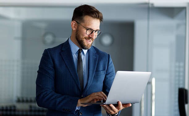 Smiling businessman working on a laptop in a modern office, confidently typing on the keyboard while enjoying a productive day